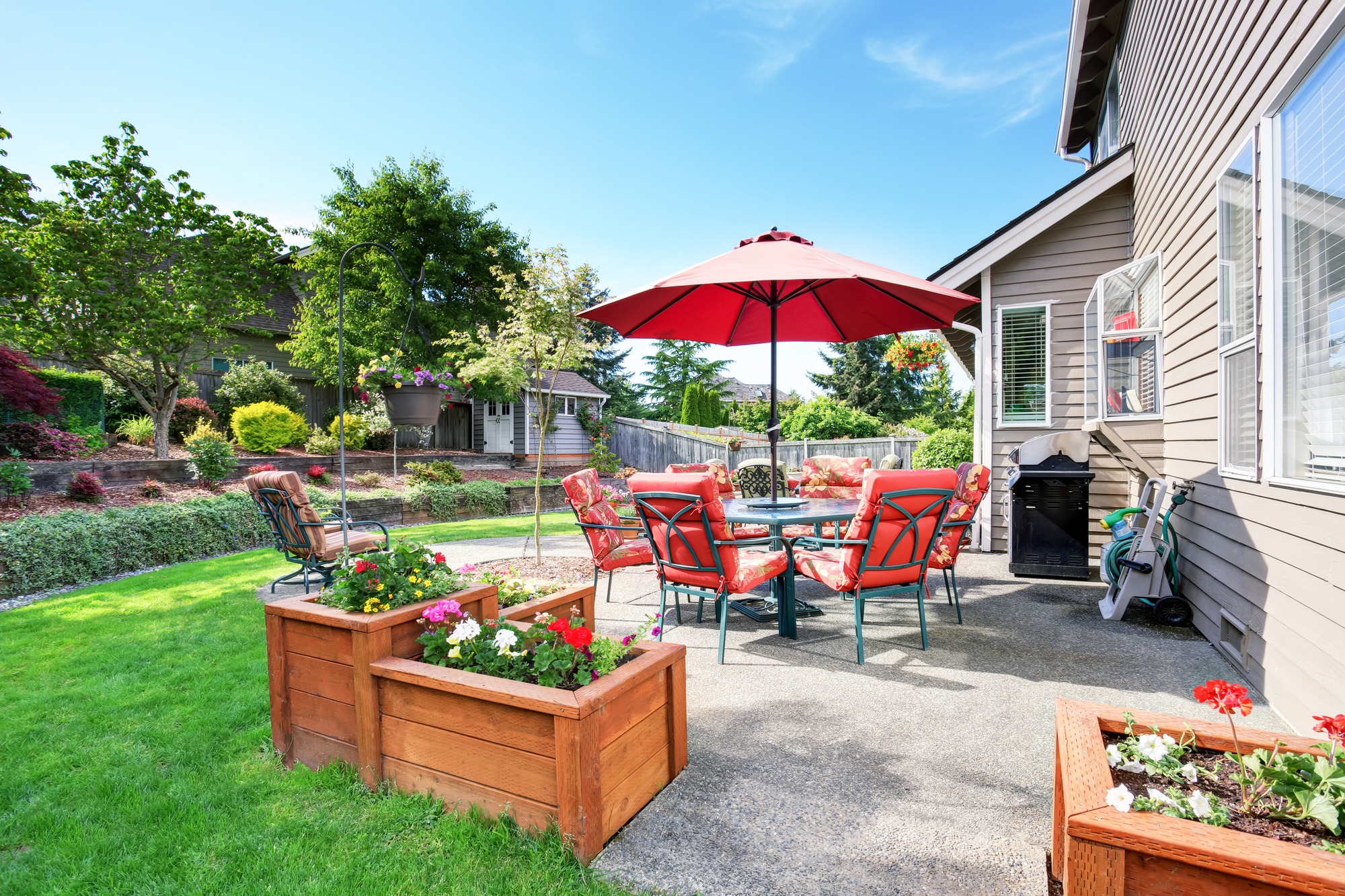 Well kept garden at backyard with concrete floor patio area and opened red umbrella. Northwest USA